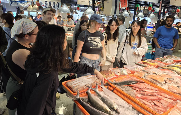 IMAS students visited various markets to select seafood for lunch; among them, American student Jacob McGee was closely examining a shark.